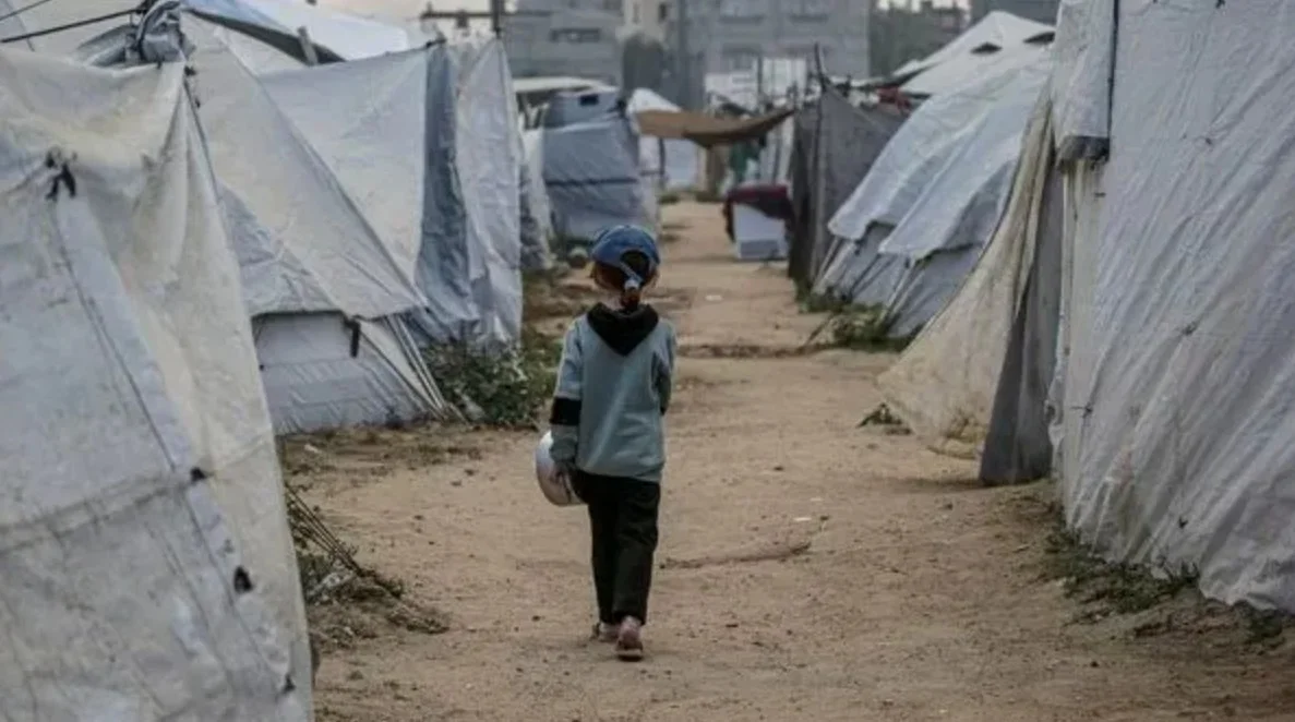 Enfant marchant entre des abris dans un camp de personnes déplacées, photographié de dos